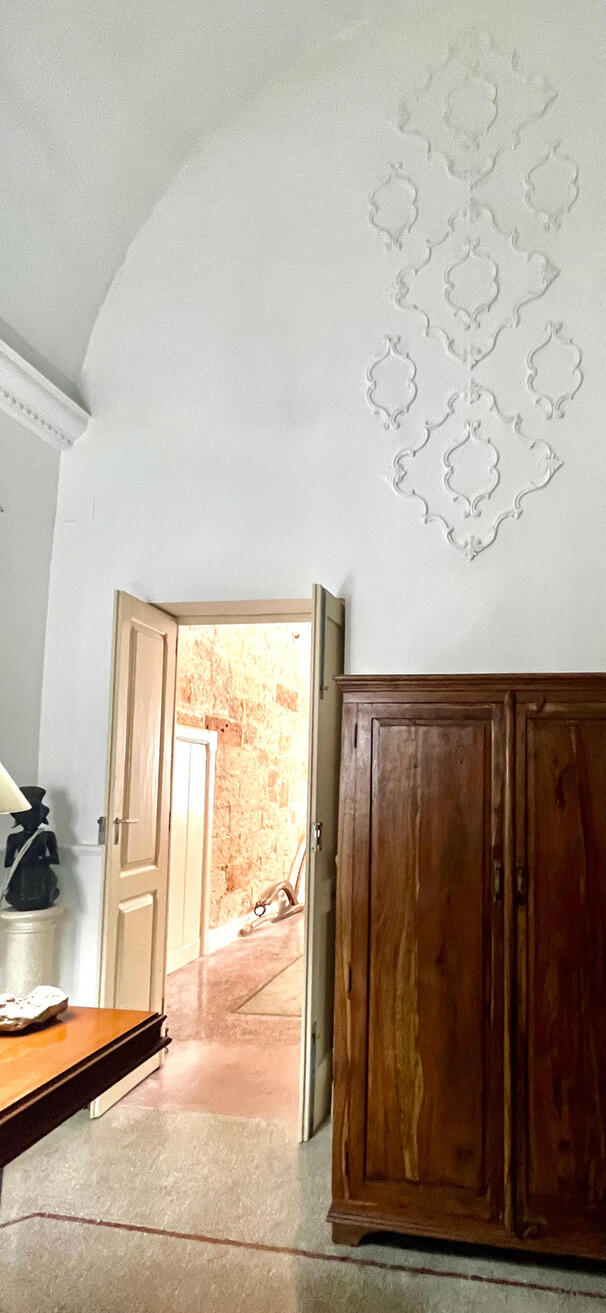 Untitled Progetto di Interior Direction in Puglia: scorcio prospettico con armadio in legno massello, decori a stucco e vista sulla stanza adiacente con pareti in tufo a vista originale. Studio 183.